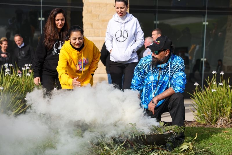Uncle Mark Brown and community members gathered around smoke and native plants